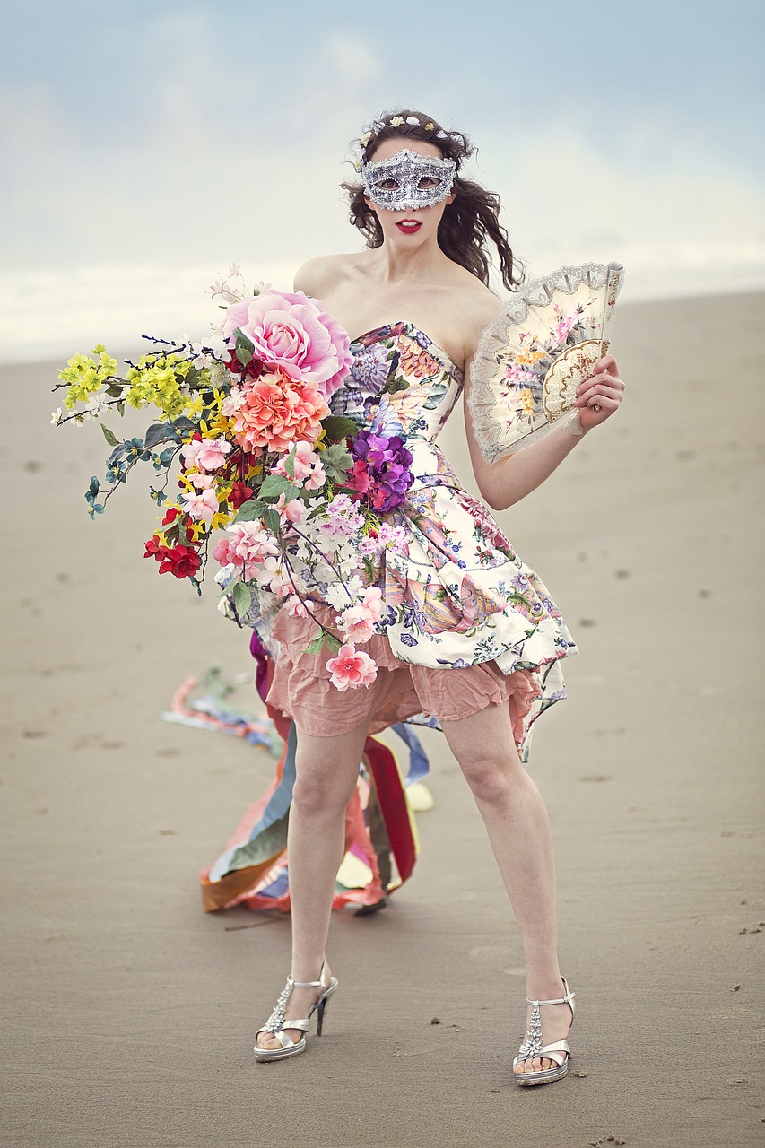 woman in sparkling mask with short floral dress and holding a fan and bouquet of flowers